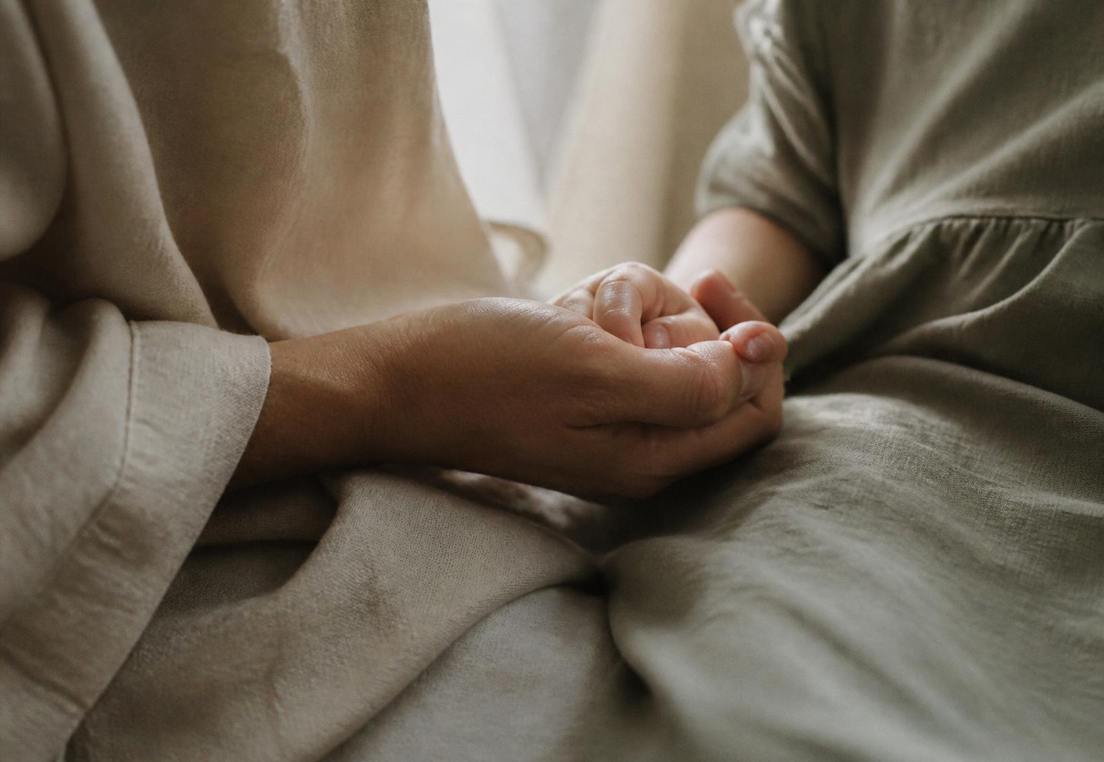 An adult hand gently holding a child's hand